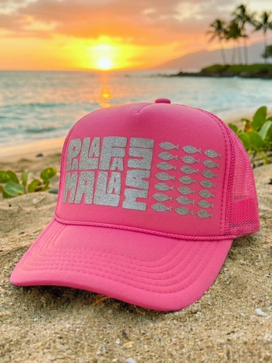 Pink cap with 'PALAFAMALA' text on a beach at sunset