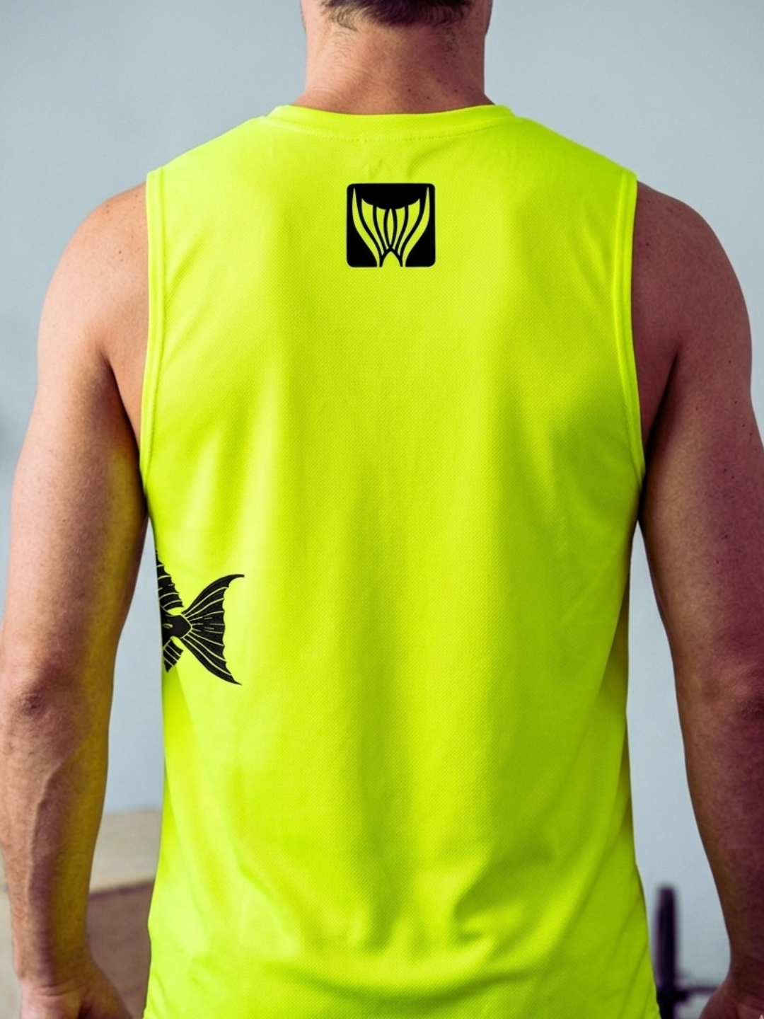 Person wearing a bright yellow sleeveless shirt with a black logo on the back against a light gray background